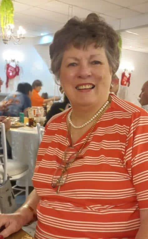 A white woman wearing an orange striped shirt and a pearl necklace.